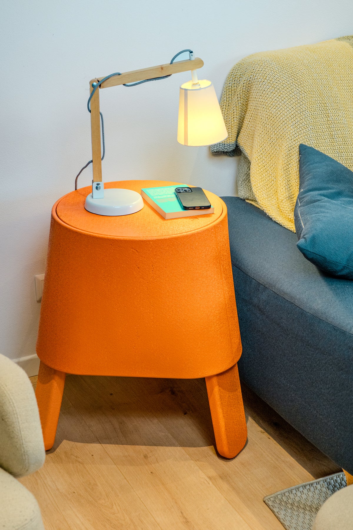 Orange AYTO as a side table with a lamp and phone next to a sofa in a living room